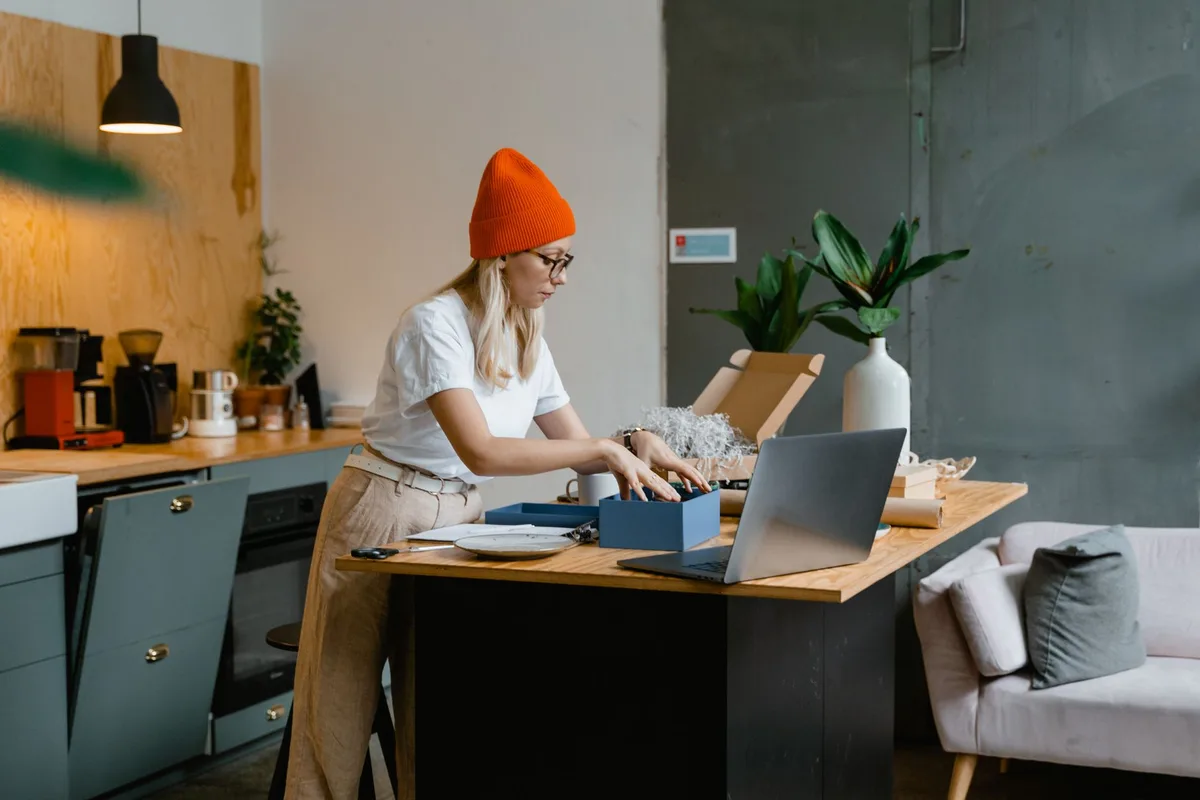 Woman setting up her dropshipping business at home with a laptop and packages on a kitchen counter