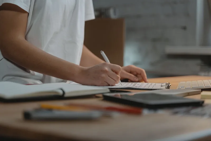 Person writing notes on a clipboard at a desk while weighing supplier options