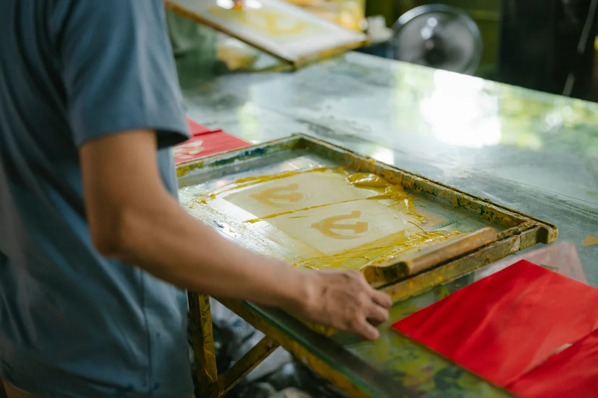 Close-up of a screen printing frame and squeegee applying custom ink onto a product design