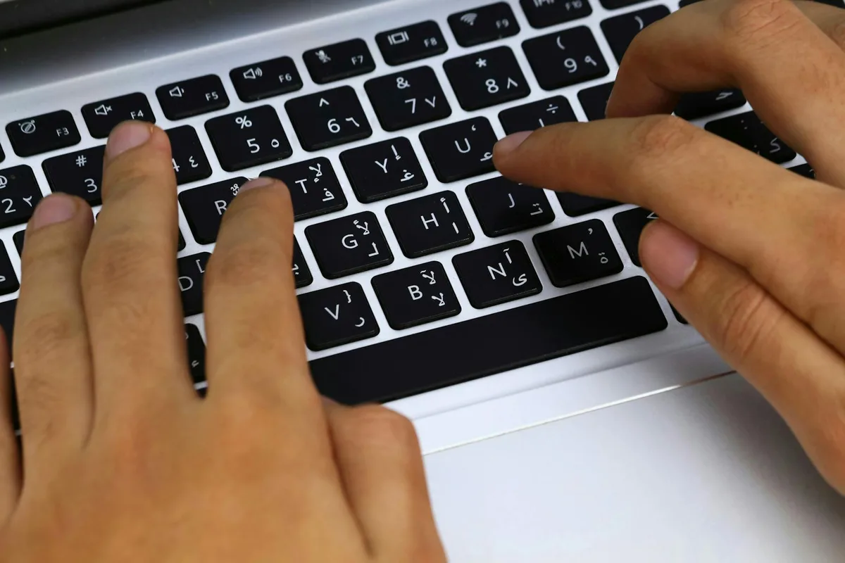 Hands typing on an Arabic layout laptop keyboard for Middle East ecommerce business