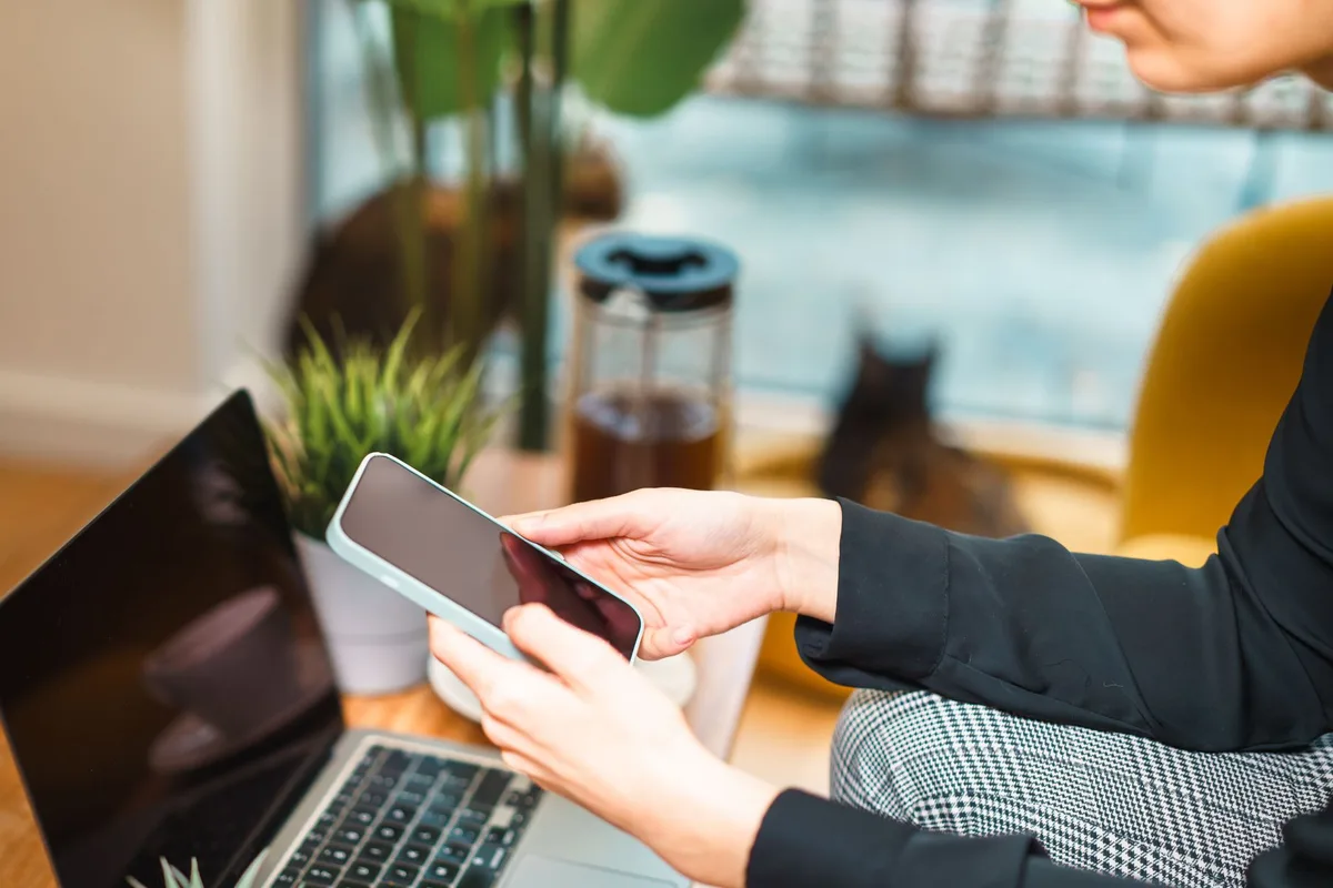Wanita bekerja dari rumah menggunakan smartphone dan laptop di meja kerja