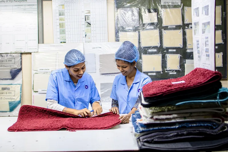 Dua pekerja pabrik tekstil memeriksa contoh karpet di meja kerja