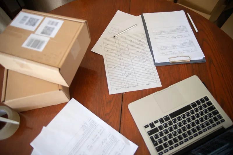 Flat-lay workspace with laptop, documents, and cardboard boxes representing a home-based ecommerce business