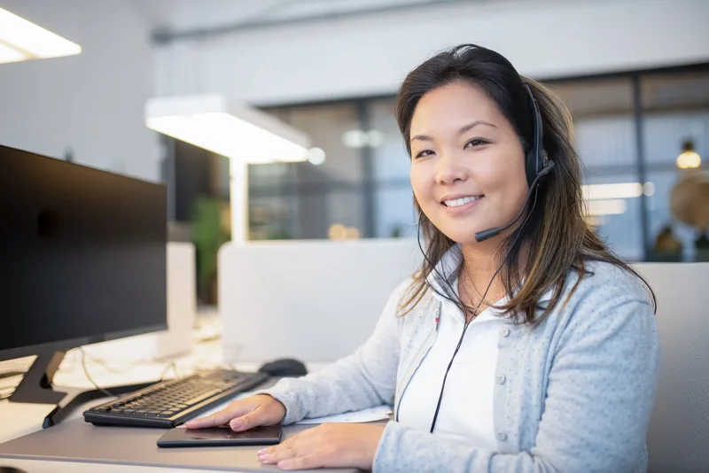 Customer support agent with a headset smiling at her desk, ready to answer seller questions