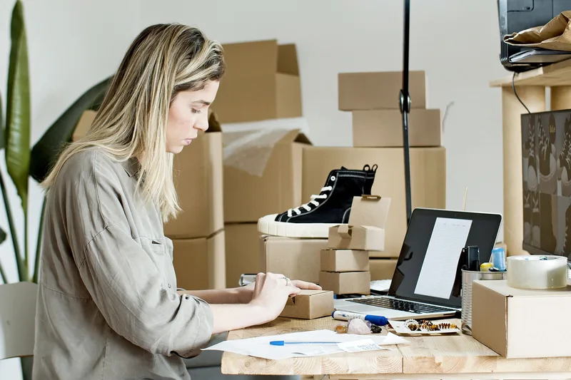 Woman packing an online store order next to a laptop