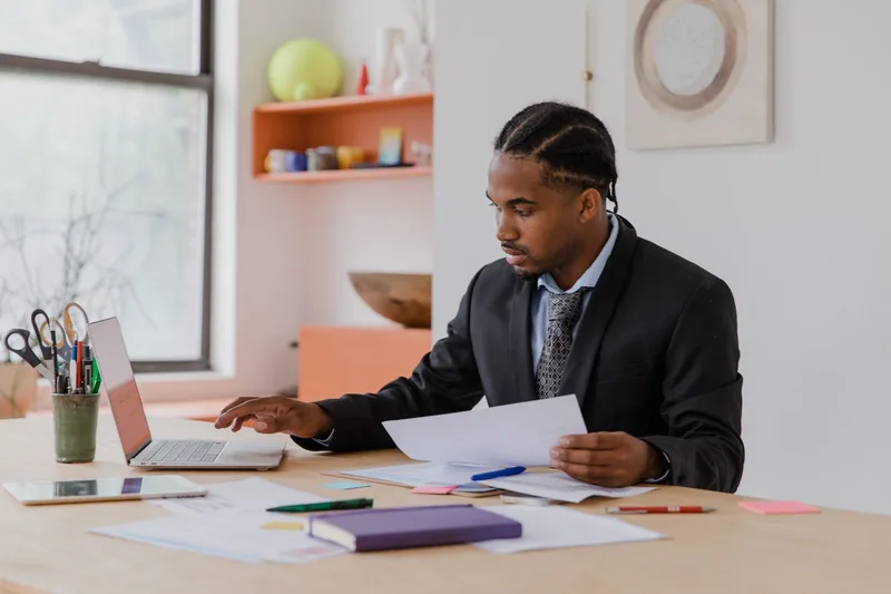 Small business owner reviewing paperwork and a laptop before submitting seller documents