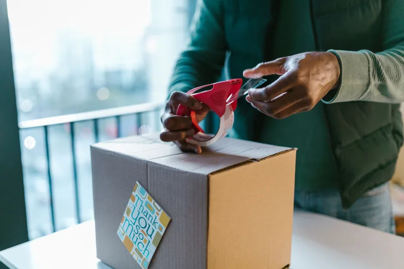 Hands sealing a shipping box with tape after packing an online order