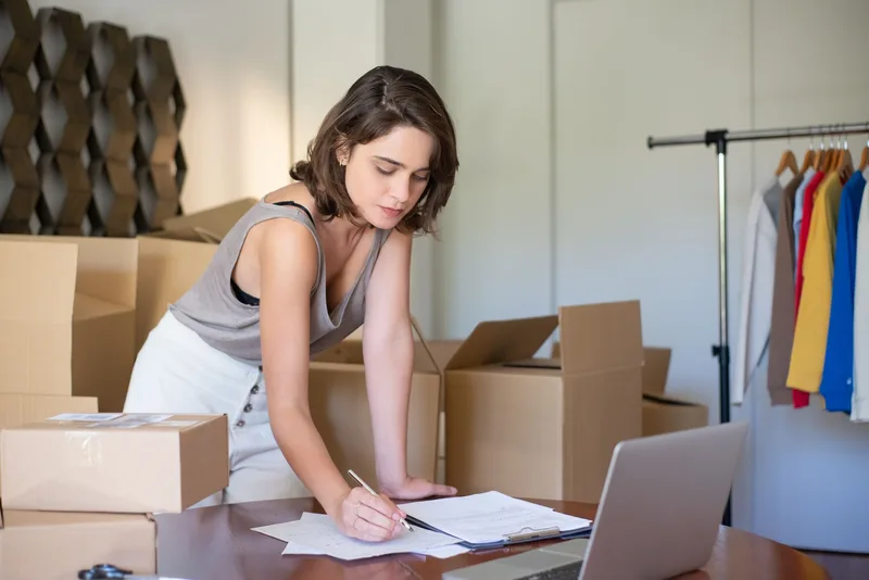 Entrepreneur setting up an online seller account on a laptop at home, surrounded by shipping boxes