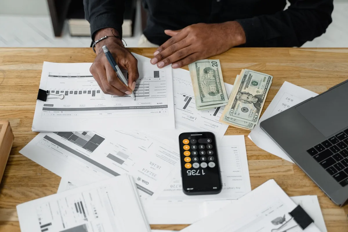 Person reviewing a laptop budget spreadsheet with a calculator and cash, planning ecommerce costs
