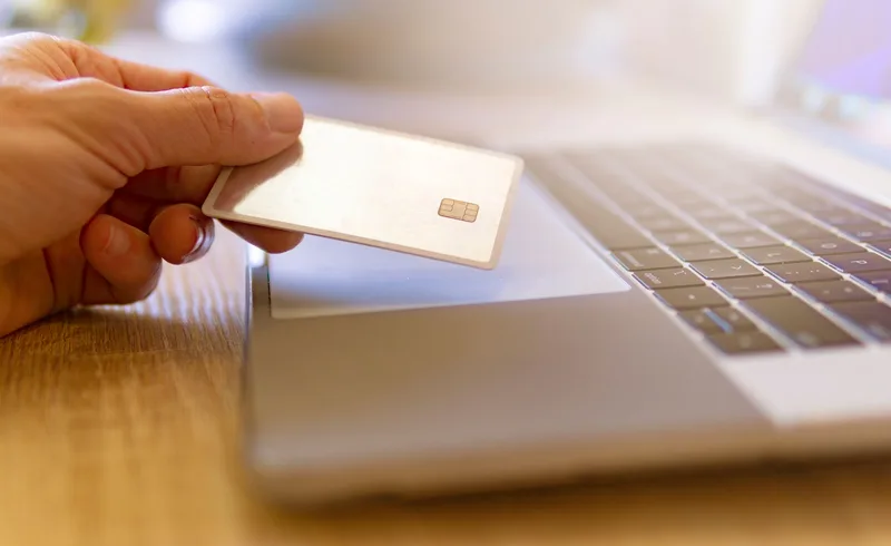 Close-up of a person using a credit card for online shopping on a laptop