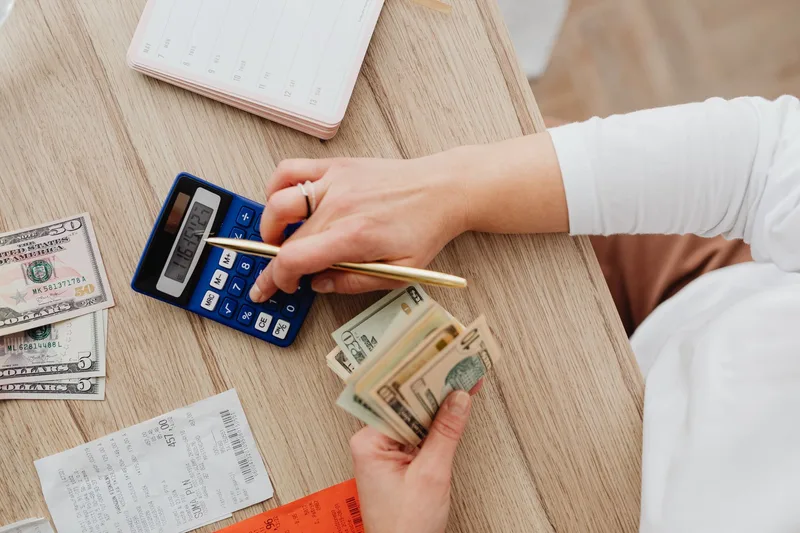 Hands managing finances with calculator, cash, and receipts on a wooden table