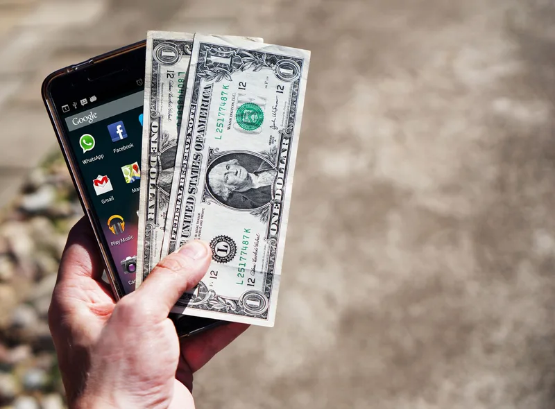 Hand holding a smartphone next to cash, representing mobile payment processing costs