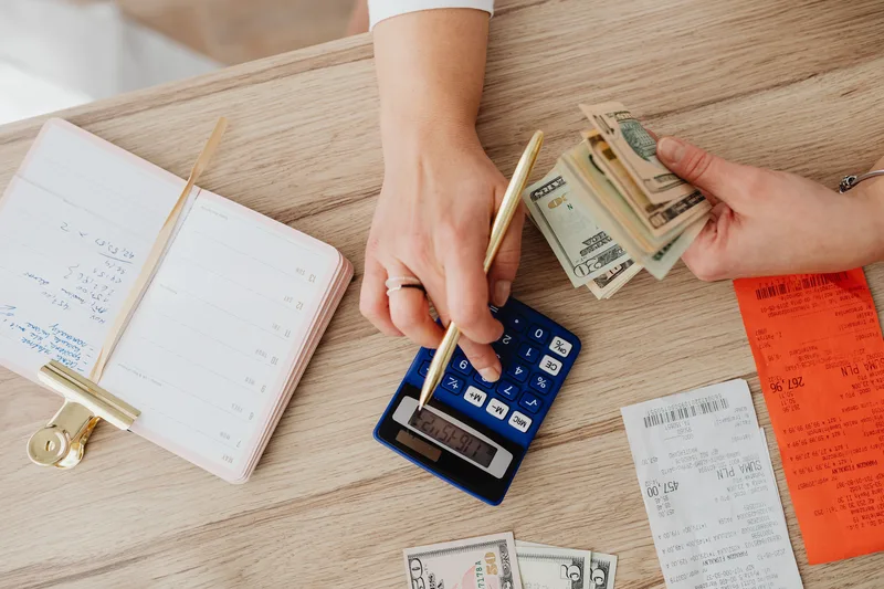 Hands managing finances with calculator, cash, and receipts on a wooden table