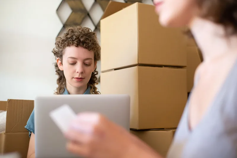 Two women managing a small business surrounded by cardboard boxes and a laptop for online orders