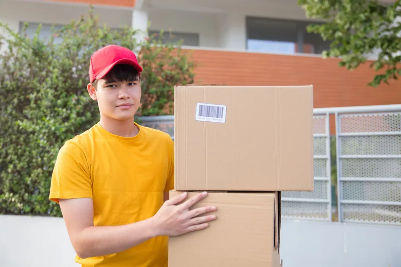 พนักงานจัดส่งถือกล่องพัสดุหลายกล่องซ้อนกัน สื่อถึงการจัดส่งสินค้าหลังลูกค้าสั่งซื้อผ่านร้านออนไลน์