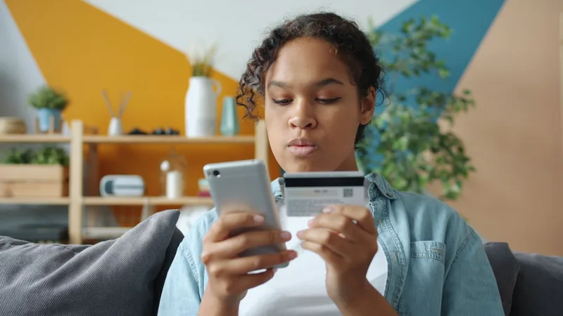 Perempuan memegang ponsel dan kartu bank untuk membayar belanja online dari rumah