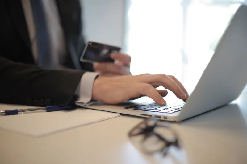 Person typing on a laptop while holding a payment card to complete an online setup
